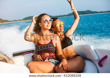 Two pretty amazing hipster girls, blond and brunette ride on a speed boat, wearing sunglasses, happy, tanned, crazy emotions, sexy bikini, fashion accessories, luxury, lifestyle waves splashes