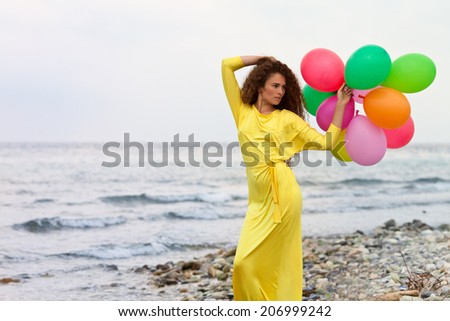 Beautiful girl in yellow long dress and long hair with balloons on the beach