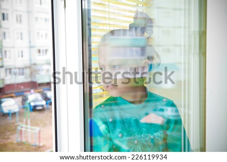 Little beautiful girl looking through an open window to the street