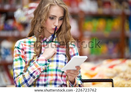 Beautiful young girl at the grocery store with a notepad and pen in hand selects products