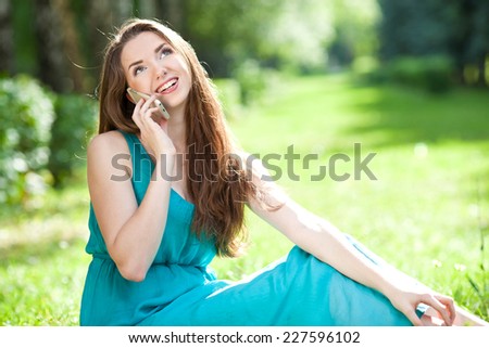 Beautiful girl with long hair in a green dress sitting on the nature and talking on cell phone