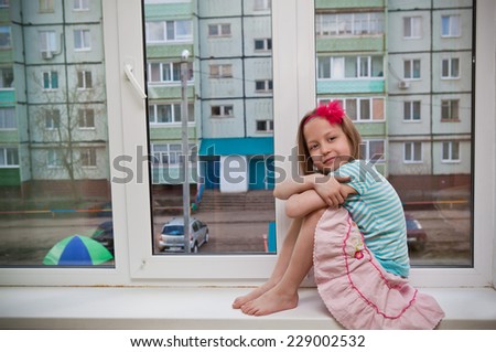 Girl looking out the open window while sitting on the windowsill in the room of the house