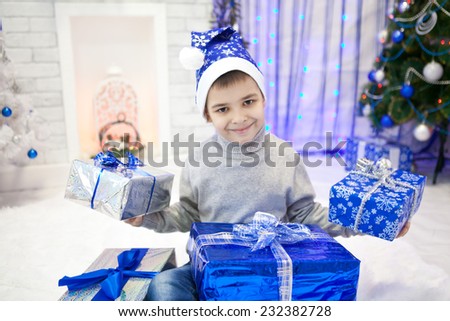 Handsome boy in blue Christmas cap holding boxes with gifts in their hands in the New Year interior