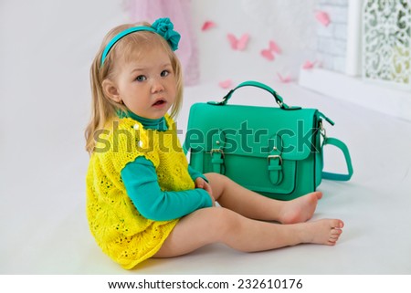 Little beautiful girl in yellow dress sitting with green bag in the room