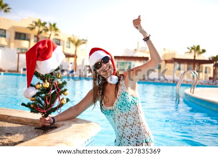 Beautiful girl in Christmas red hat with a Christmas tree in the summer resting by the pool