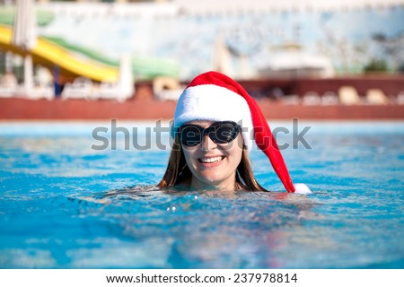 Beautiful girl swimming in pool summer day with a red santa hat on head