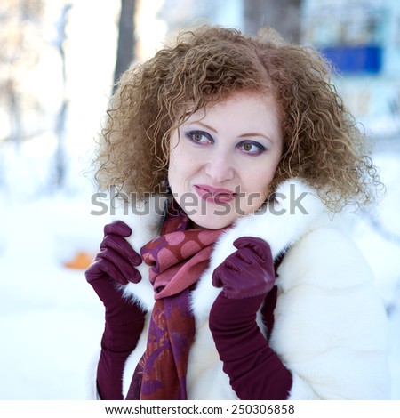 Young woman in white mink coat and red scarf walking on the street in winter