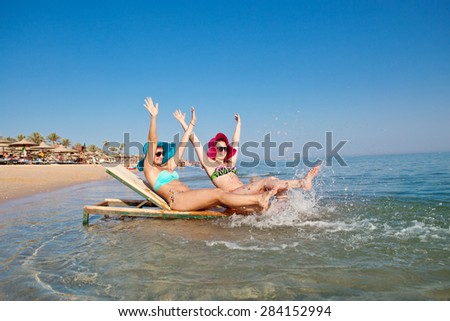 Two beautiful happy girls in bright panama hats splashing on the shore of the Red Sea on vacation