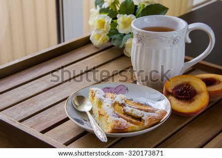 piece of peach pie on a white plate, white mug with tea on a wooden surface and yellow flowers in the background, natural light from the window. Horizontal photo