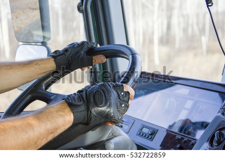 Closeup view from the truck. Truck driver driving wheel with both hands in driving gloves