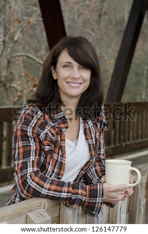 Pretty lady drinking coffee on an old wooden bridge