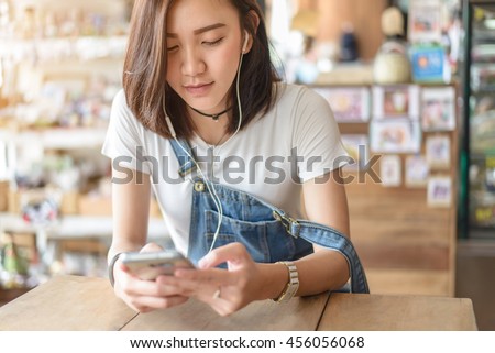 Cute asian girl listening by earphone and look at smartphone in hand