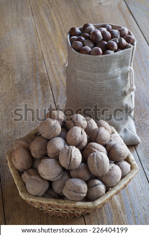 Walnuts in a wicker basket and hazelnuts in a cotton bag on a wooden table.