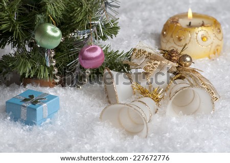 In the snow near the Christmas tree are bells, blue gift box and burning candle.