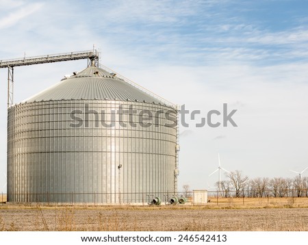 Grain bin with wind turbines in the background on a farm