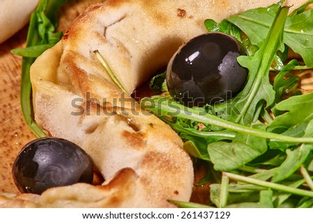 Freshly baked crispy bread strings mixed with black olives and rucola on wooden platter