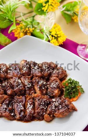 Salty-sweet grilled Korean beef dish (Bulgogi) topped with toasted sesame seeds. Top view, arranged on a tabletop against a bright purple place mat and yellow flowers in the background.