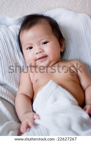 Smiling baby lying in bed under blanket