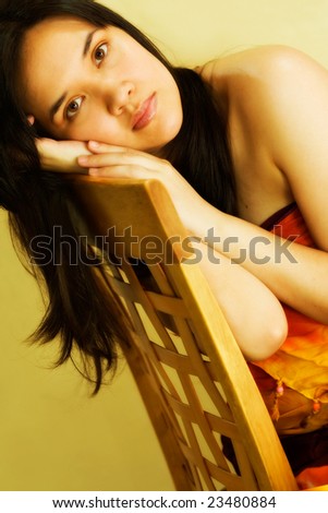 Woman resting her face on hands, leaning on chair. Very warm tones.
