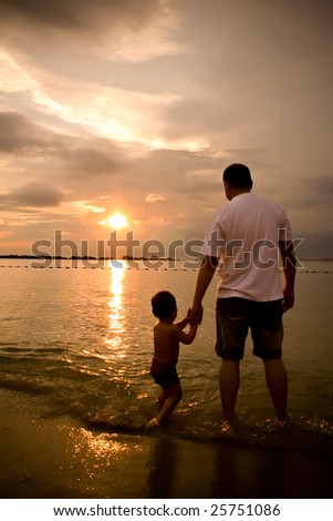 Father and son on beach shore during sunset, holding hands