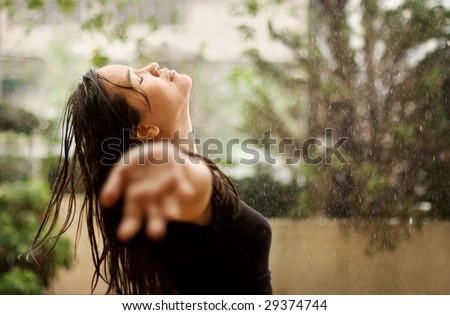 Woman standing under the rain, eyes closed and arms raised. Available space for text on the right side.
