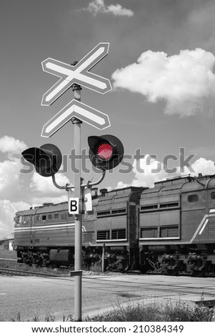 Railroad crossing with passing freight train - black and white with a red signal light