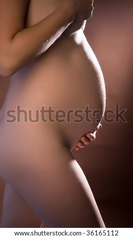 stock photo Young naked pregnant woman on brown ground