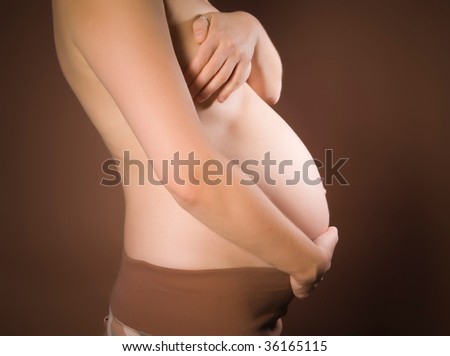 stock photo Half naked pregnant woman holding her belly on brown ground