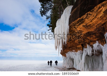 Frozen Lake Superior shoreline.  Orange cliff, large icicles, people for scale.  Copy space.  Apostle Islands National Lakeshore on Lake Superior.  Popular winter travel destination.