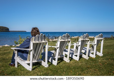 Lady sitting in one of four beach chairs in the Autumn looking at the horizon.  Shot in Door County, Wisconsin.  Copy space on top half of frame.