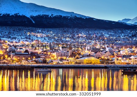 Ushuaia city in the late afternoon/night, lights on, lake in the foreground and snowed mountains in the background. Argentina, Patagonia, South America