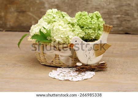 Shabby chic style spring composition with wooden bird decoration and a cute basket with fresh flowers on a grungy background