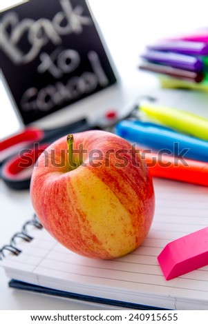 bright colored back to school supplies and an apple for the teacher
