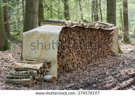 Tree logs piled up under a roll covering in a forest