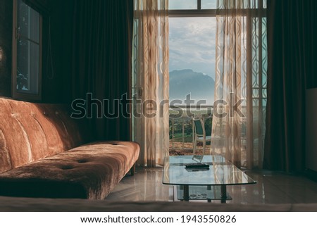 Brown sofa and White curtain by the window and view of the mountain with light from the sunset, Beautiful curtain make the house more livable, Relaxation at living room in a holiday close to nature.