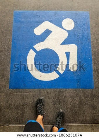 Handicapped sign on a parking space with feet of a man wearing black shoes