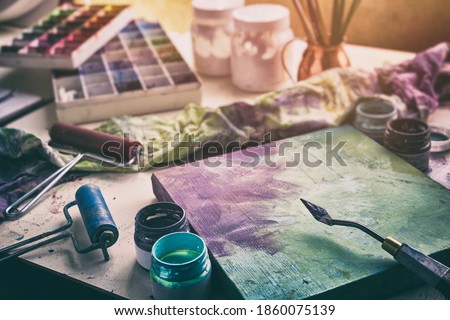 Artistic equipment - canvas and palette knife, paint brushes, multicolored paints in artist studio.