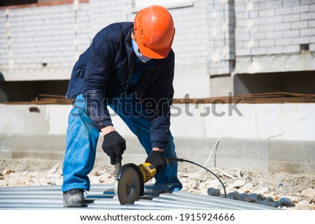 The builder uses an electric grinding machine to cut the profiled flooring
