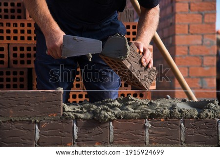 Bricklayer worker installing brick masonry on exterior wall. Professional construction worker laying bricks.