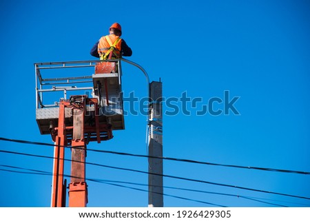 Worker with helmet and safety protective equipment installs new diode lights. Worker in lift bucket repair light pole. Modernization of street lamps.