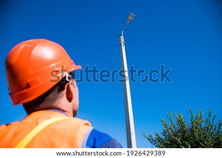 Worker with helmet and safety protective equipment installs new diode lights. Worker in lift bucket repair light pole. Modernization of street lamps.