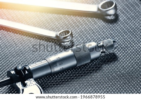 A closeup of a mechanical micrometer and open-end wrenches lying on a steel table.