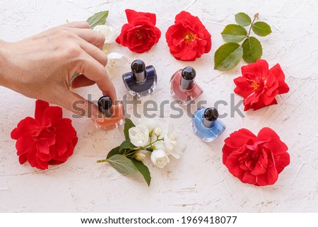 Bottles with nail polish on a white background with buds of rose flowers. Woman\'s hand with a bottle of nail polish. Top view.