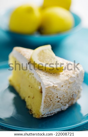 slice of lemon pie with lemons in the background, focus is on the front of the cake