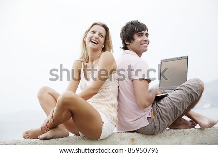 young couple sitting on a wall each with their own piece of technology