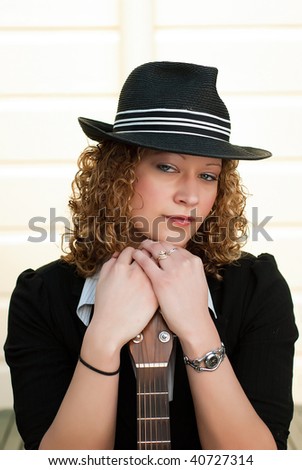 Beautiful blonde woman in hat posing with a guitar