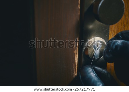 close up of a burglar with gloves picking a lock