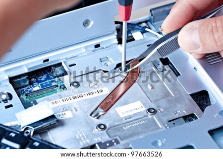 macro of a hand holding tweezers on a laptop screw