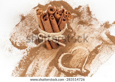 Tied bunch of cinnamon sticks and Heart shape hand drawn in cinnamon powder on white background