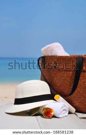 hat, bag, sun glasses and towel on a tropical beach with blue sky